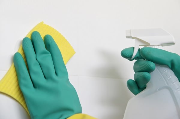 Person wearing protective plastic gloves clean bathroom tails with cleaning material and a sponge